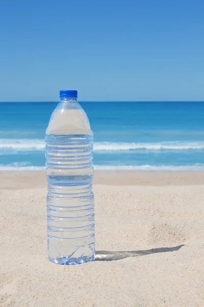 Una botella de agua fresca en la playa cerca del mar. — Foto de Stock