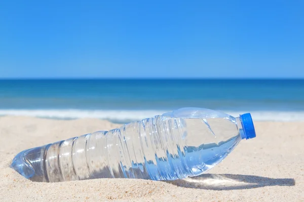 Uma garrafa de água fresca na praia perto do mar. — Fotografia de Stock