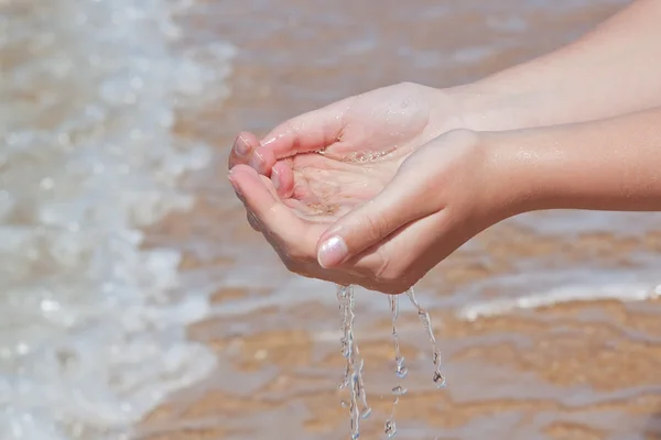 De handen nemen water naar de zee. op het strand. — Stockfoto