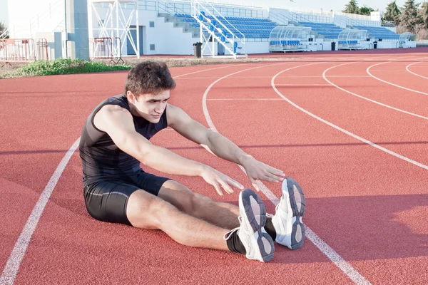 Um jovem faz um atleta alongamento. contra o pano de fundo — Fotografia de Stock