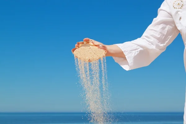 Een meisje giet zand uit de schelpen. tegen de achtergrond van de — Stockfoto