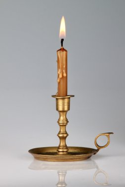 Lighted candle in an old brass candlestick, with a gray backgrou clipart