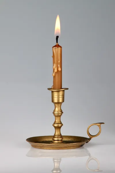 stock image Lighted candle in an old brass candlestick, with a gray backgrou