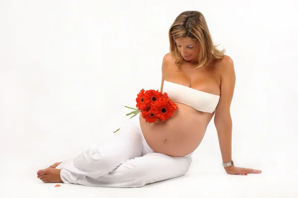 Schwangere sitzt mit roten Blumen auf dem Boden — Stockfoto