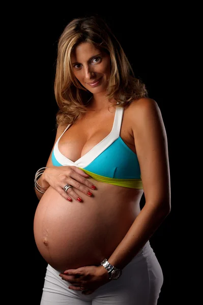 Těhotná žena při pohledu na fotoaparát drží její břicho — Stock fotografie