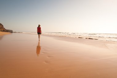 Solitary girl walking on the beach clipart