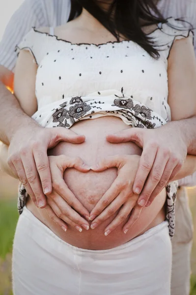 Пара делает сердечный знак на беременном животе — стоковое фото