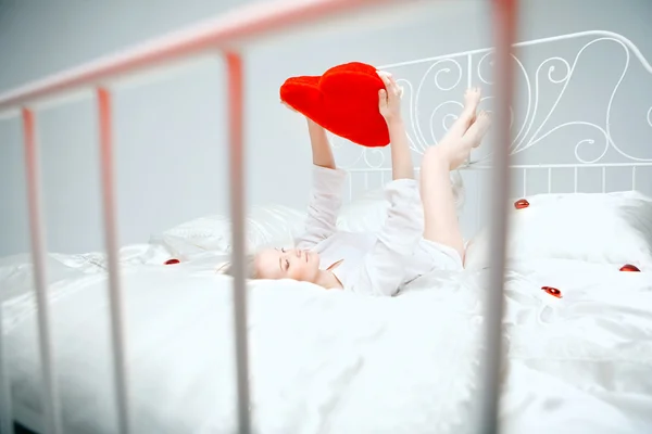 Girl lying on the bed with a red heart — Stock Photo, Image