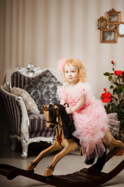 Niño en un vestido rosa en un caballo de juguete — Foto de Stock