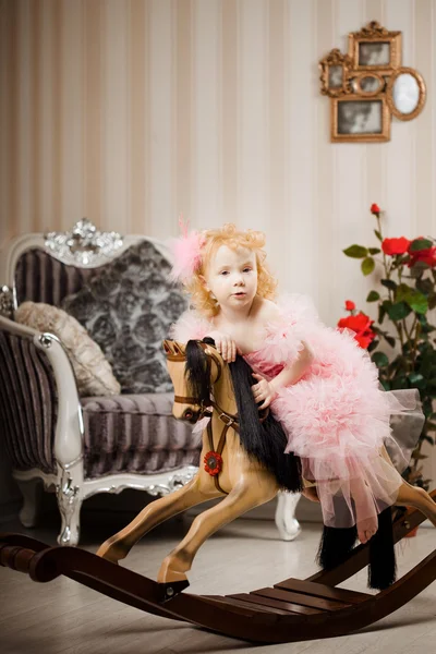 Дитина в рожевій сукні на іграшковому коні — стокове фото