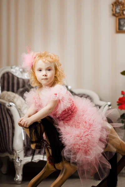Hild im rosa Kleid auf einem Spielzeugpferd — Stockfoto