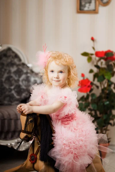 Filhote de cachorro em um vestido rosa em um cavalo de brinquedo — Fotografia de Stock