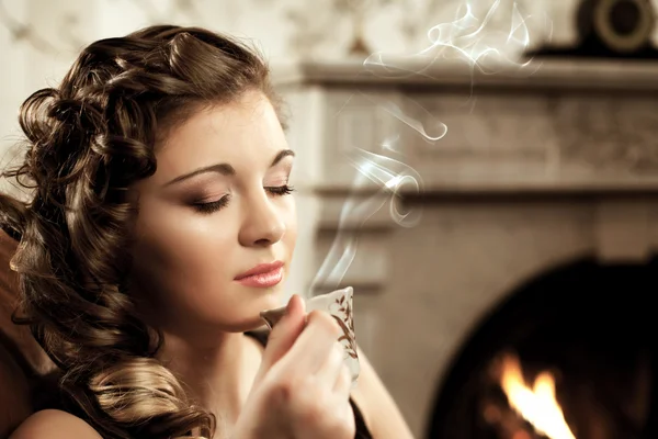 Girl drinking coffee by the fireplace — Stock Photo, Image