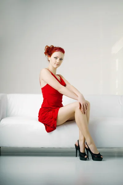 Redhead woman in a red dress on white couch — Stock Photo, Image