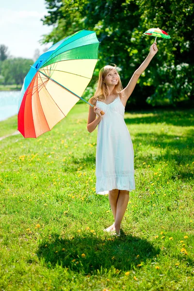 Lachende vrouw kiest voor groot of klein regenboog paraplu buitenshuis — Stockfoto