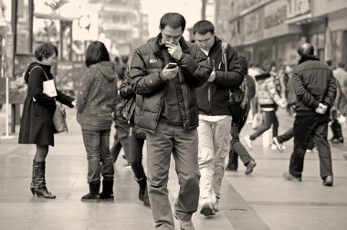 Two men using mobile phone on a busy pedestrian shopping street clipart