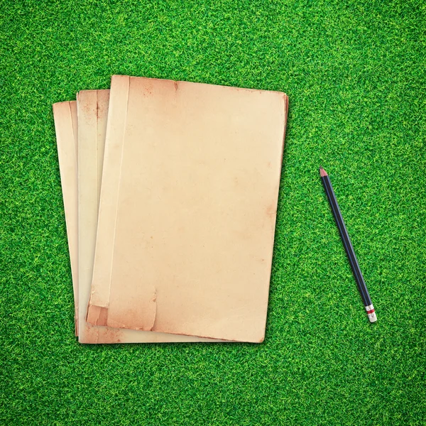 Lápis e livro velho sobre fundo grama verde — Fotografia de Stock