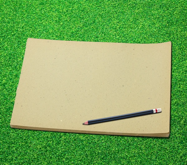 Карандаш и старая пустая книга эскизов на зеленом фоне травы — стоковое фото