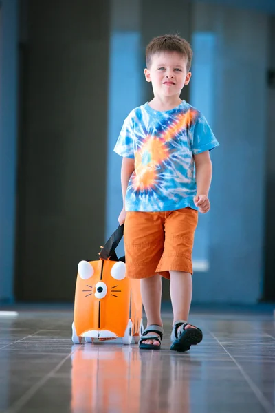 Ładny chłopczyk z walizce pomarańczowy na lotnisku — Zdjęcie stockowe