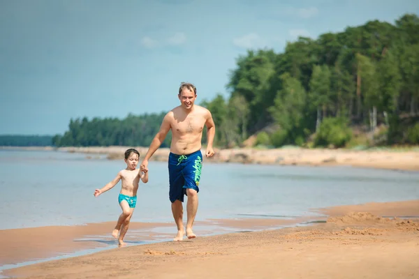 Vader en zijn kind loopt langs het strand — Stockfoto