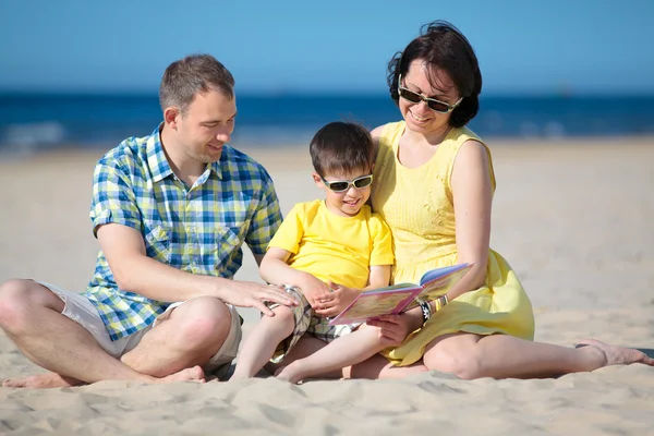 Family of three reading book on beach — Stock Photo, Image