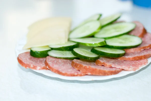 stock image Dish with cut sausage, cheese and a cucumber