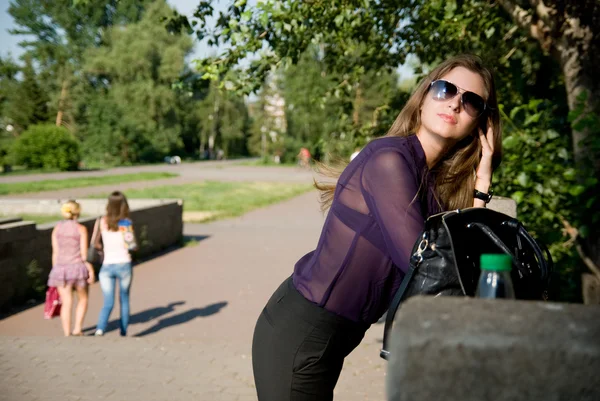 Mooi meisje met een handtas en donkere glazen in park — Stockfoto