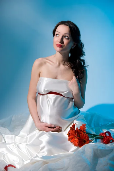 Kobieta w ciąży siedzi z kwiatami na tkaninie — Zdjęcie stockowe