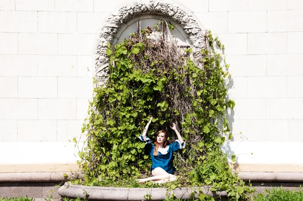Krásná rusovlasá dívka sedí v oblouku zelené šlahouny. — Stock fotografie