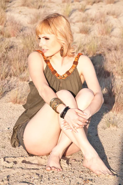 Beautiful blonde in a khaki shirt sitting cross-legged on sand — Stock Photo, Image