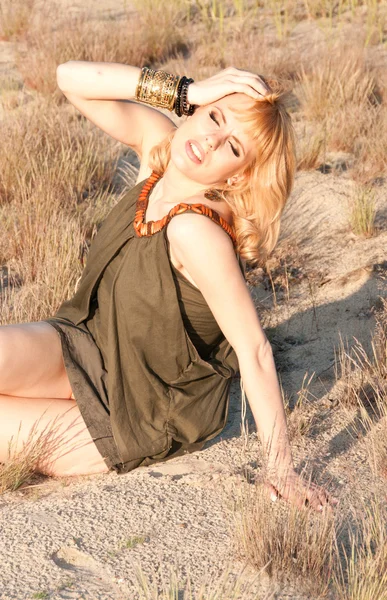 Beautiful blonde in a khaki shirt sitting on the sand — Stock Photo, Image