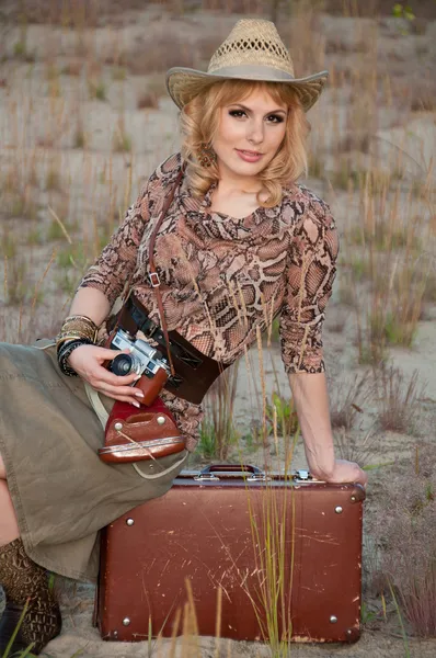 A girl travels in a cowboy hat, with a camera and a suitcase in — Stock Photo, Image