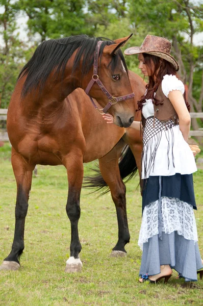 A pretty girl in a cowboy hat stroking a horse — Stock Photo, Image