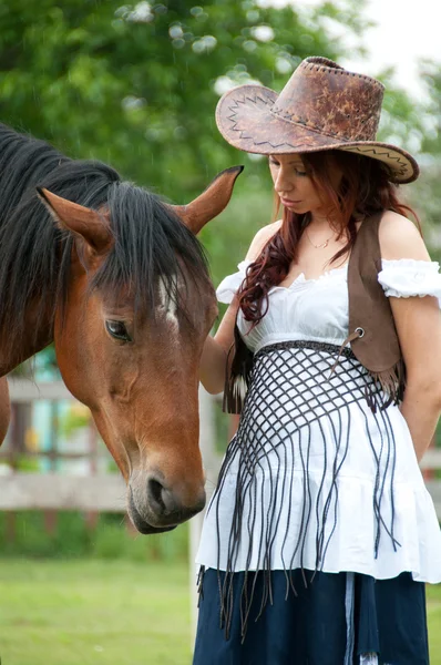 Красивая девушка в ковбойской шляпе гладит лошадь — стоковое фото