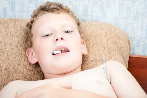 Un adolescente con una tableta en la boca, mide la temperatura —  Fotos de Stock