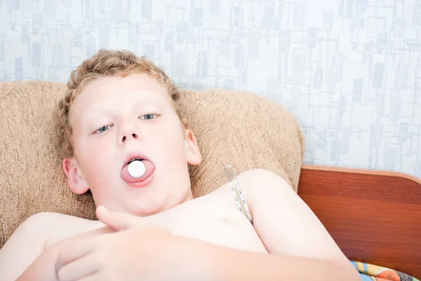 En tonåring med en tablett i hans mun, mäter temperaturen — Stockfoto