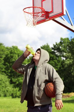 Man holding basketball and drink from bottle of water clipart