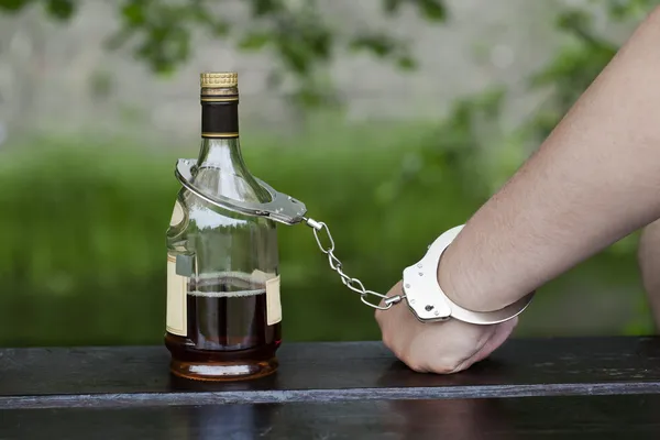 Человек в наручниках, связанный с бутылкой алкоголя — стоковое фото