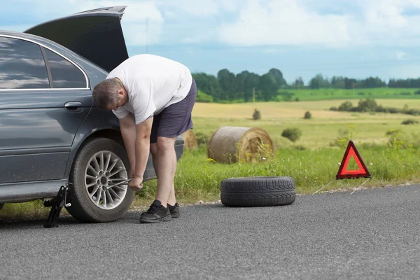 Hombre cambiando neumático en el camino —  Fotos de Stock