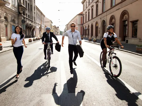 Businesspeople riding on bikes and running in city — Stock Photo, Image