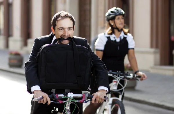 Empresário e mulher correndo em bicicletas - homem segurando mala na boca — Fotografia de Stock