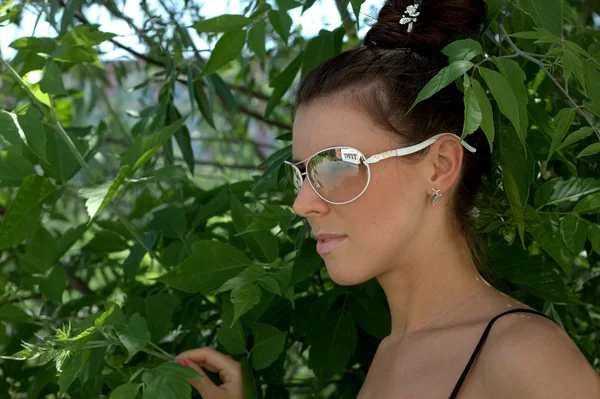 The beautiful girl in dark glasses against foliage — Stock Photo, Image