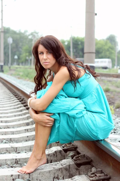 A bela menina de cabelos escuros em um vestido azul senta-se em trilhos — Fotografia de Stock