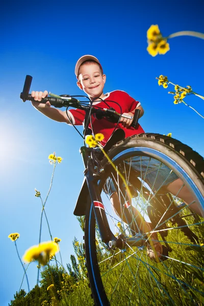 Jongen met fiets staande tegen de blauwe hemel — Stockfoto
