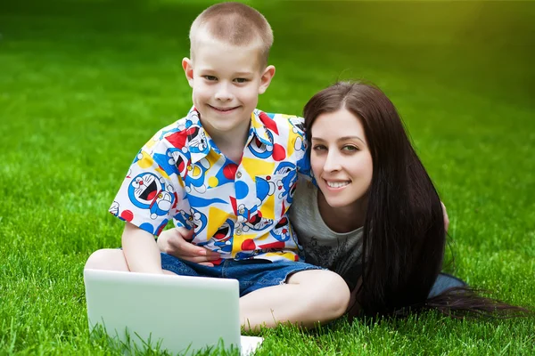 Zâmbind mama și fiul întinzându-se pe iarbă cu laptop — Fotografie, imagine de stoc