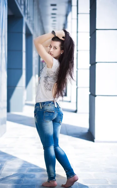 Chica bonita en jeans posando contra un edificio moderno — Foto de Stock