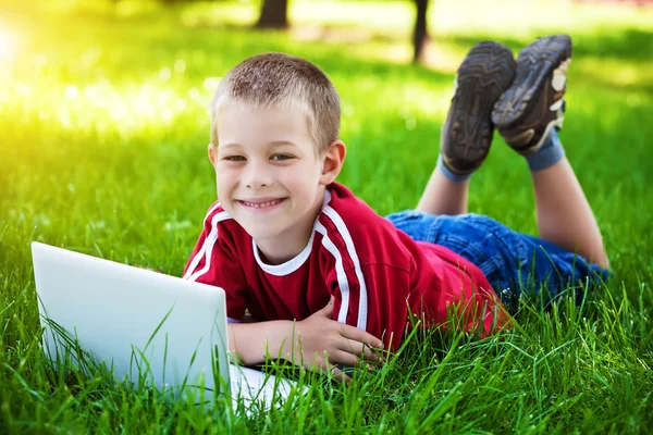 Usměvavý chlapec sedí s notebookem v trávě — Stock fotografie