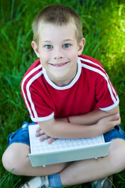 Menino sentado com um laptop na grama — Fotografia de Stock