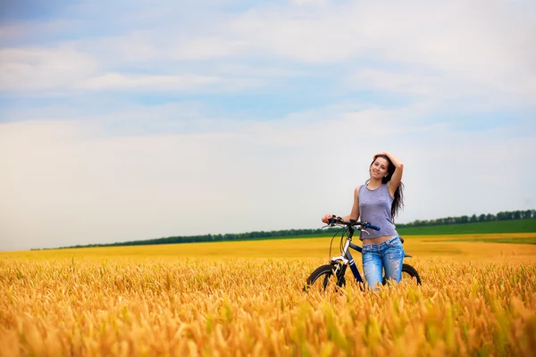 Schönes Mädchen mit Fahrrad auf dem gelben Weizenfeld — Stockfoto