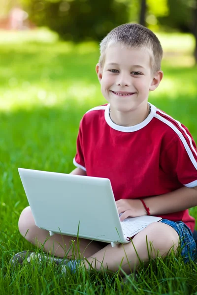 Αγόρι καθιστός με ένα φορητό υπολογιστή στο γρασίδι — Φωτογραφία Αρχείου